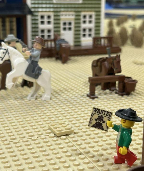 LEGO minifigura körözési hirdetménnyel, háttérben lovasok