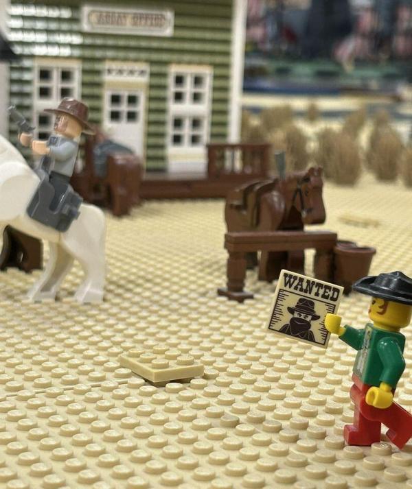 LEGO minifigura körözési hirdetménnyel, háttérben lovasok